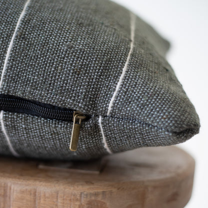 Gray woven pillow with black zipper detail resting on wooden base, close-up of fabric texture and closure.