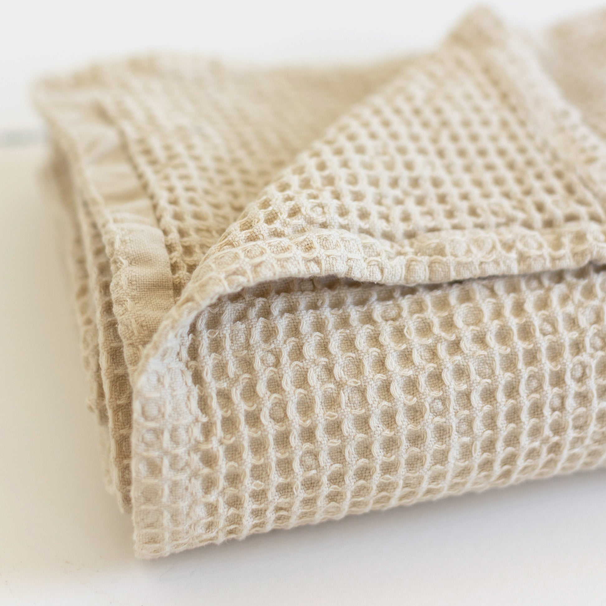Ivory waffle-textured blanket folded with visible square grid pattern and binding trim.