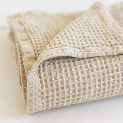 Ivory waffle-textured blanket folded with visible square grid pattern and binding trim.