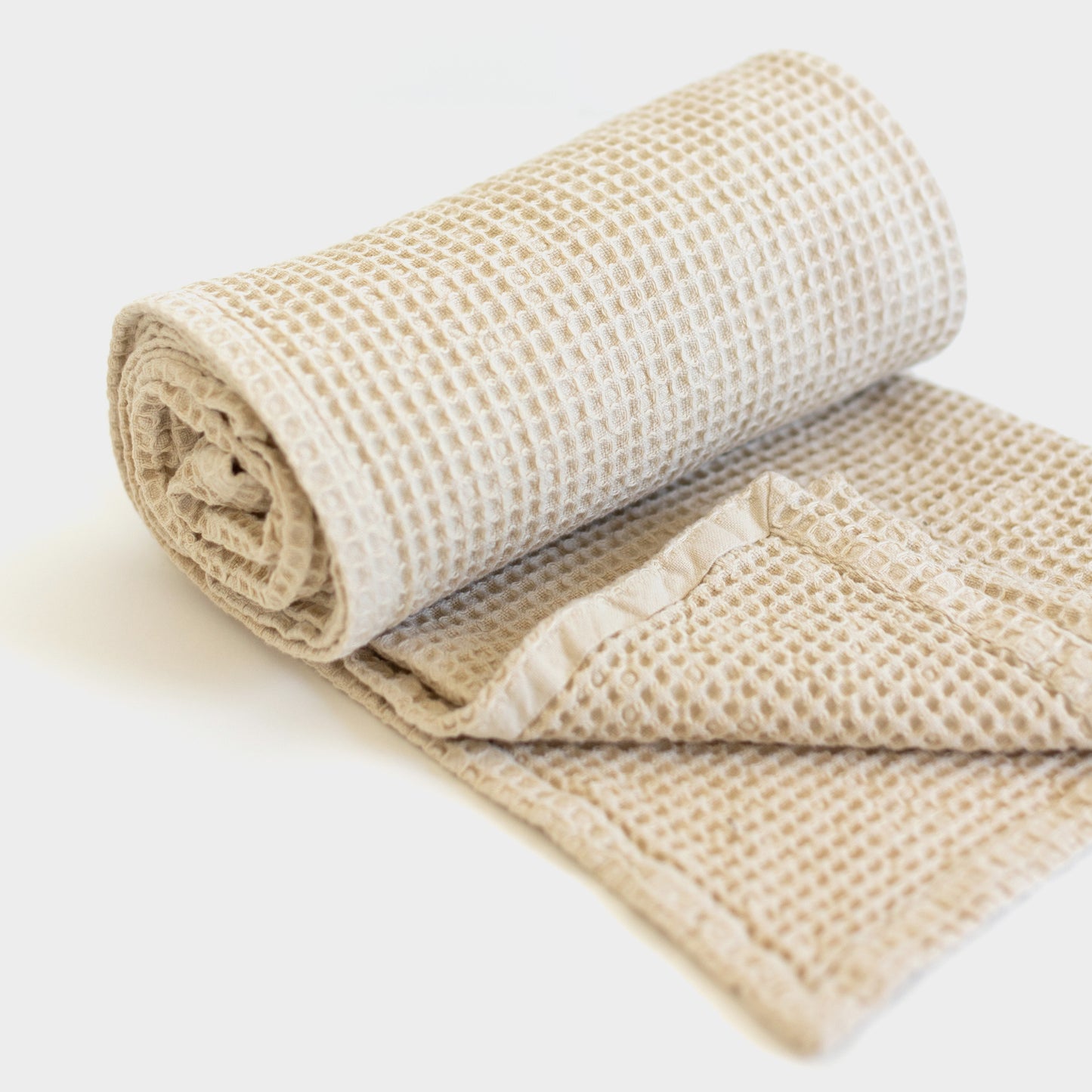 Ivory waffle-weave blanket rolled and partially unfolded, showing textured grid pattern throughout.