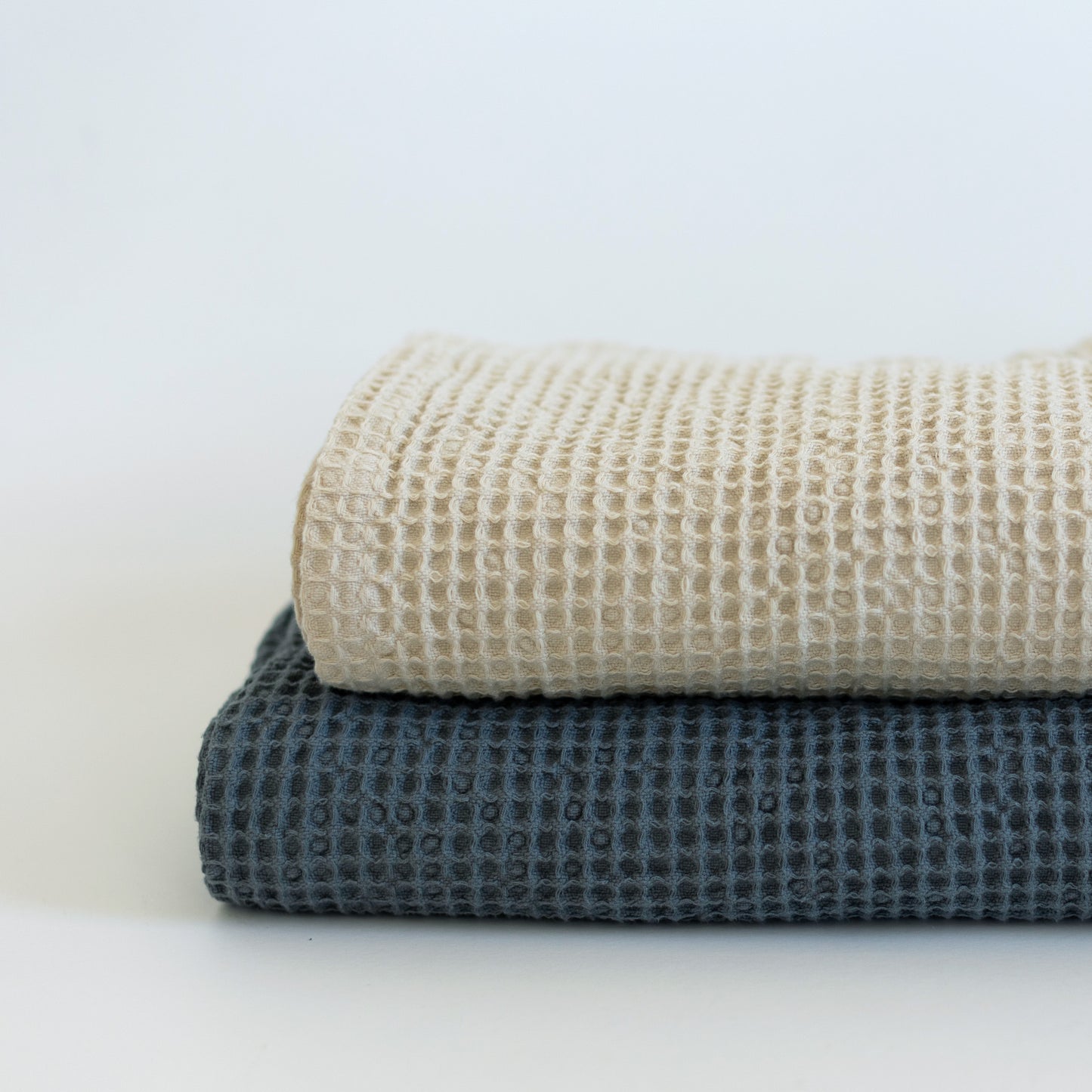 Ivory waffle-weave blanket folded on top of a charcoal gray blanket, showing textured fabric detail.