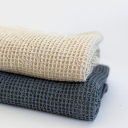 Ivory waffle-textured blanket folded with a dark gray blanket underneath.