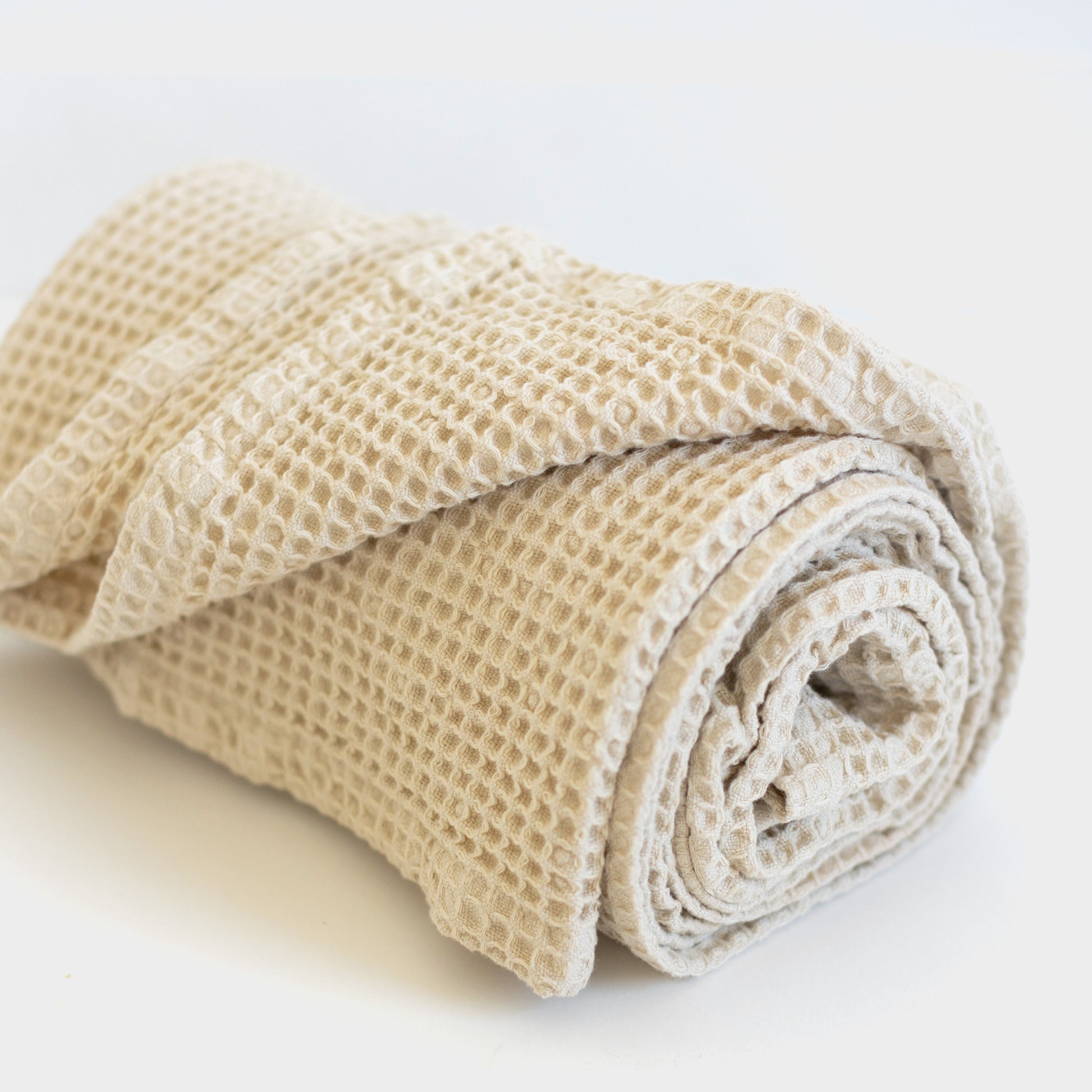 Ivory waffle blanket rolled and stacked, showing textured woven pattern.