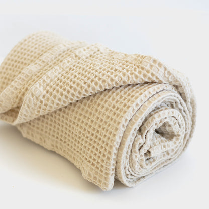 Ivory waffle blanket rolled and stacked, showing textured woven pattern.