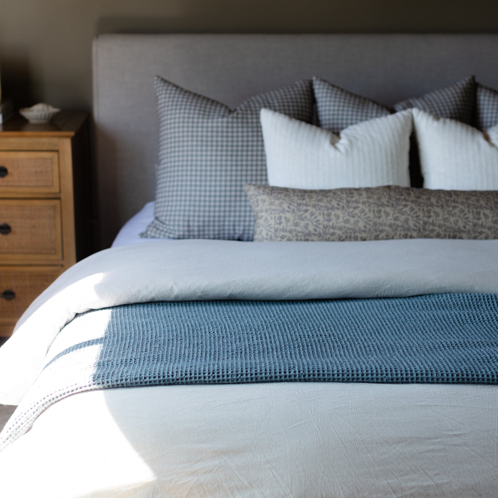 Storm blue waffle-textured blanket draped across a bed with white and patterned pillows.