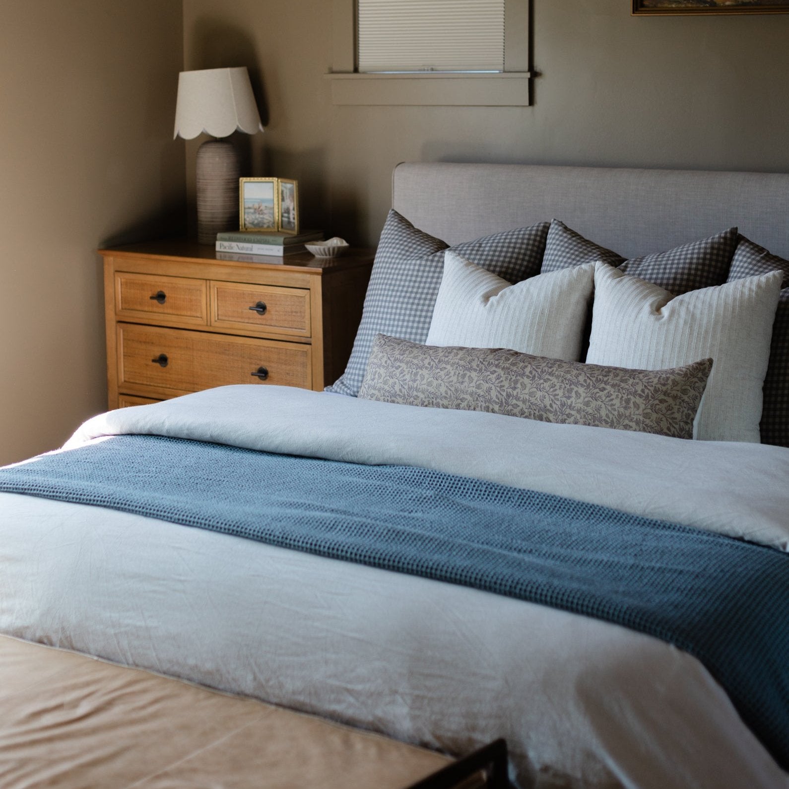 Blue waffle-textured blanket draped across a bed with white bedding and patterned pillows.