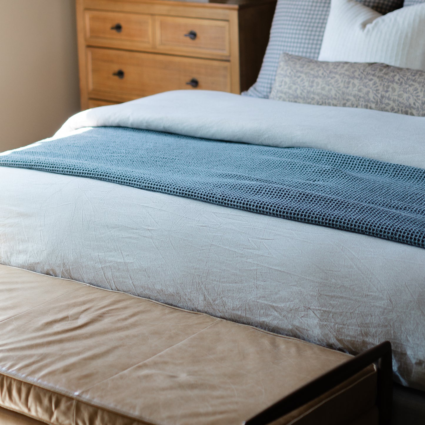 Storm blue waffle-textured blanket draped across a bed with white and gray bedding.