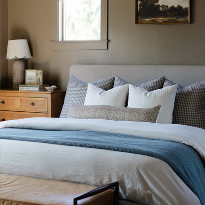Storm blue waffle-textured blanket draped across a bed with white pillows and gray bedding.