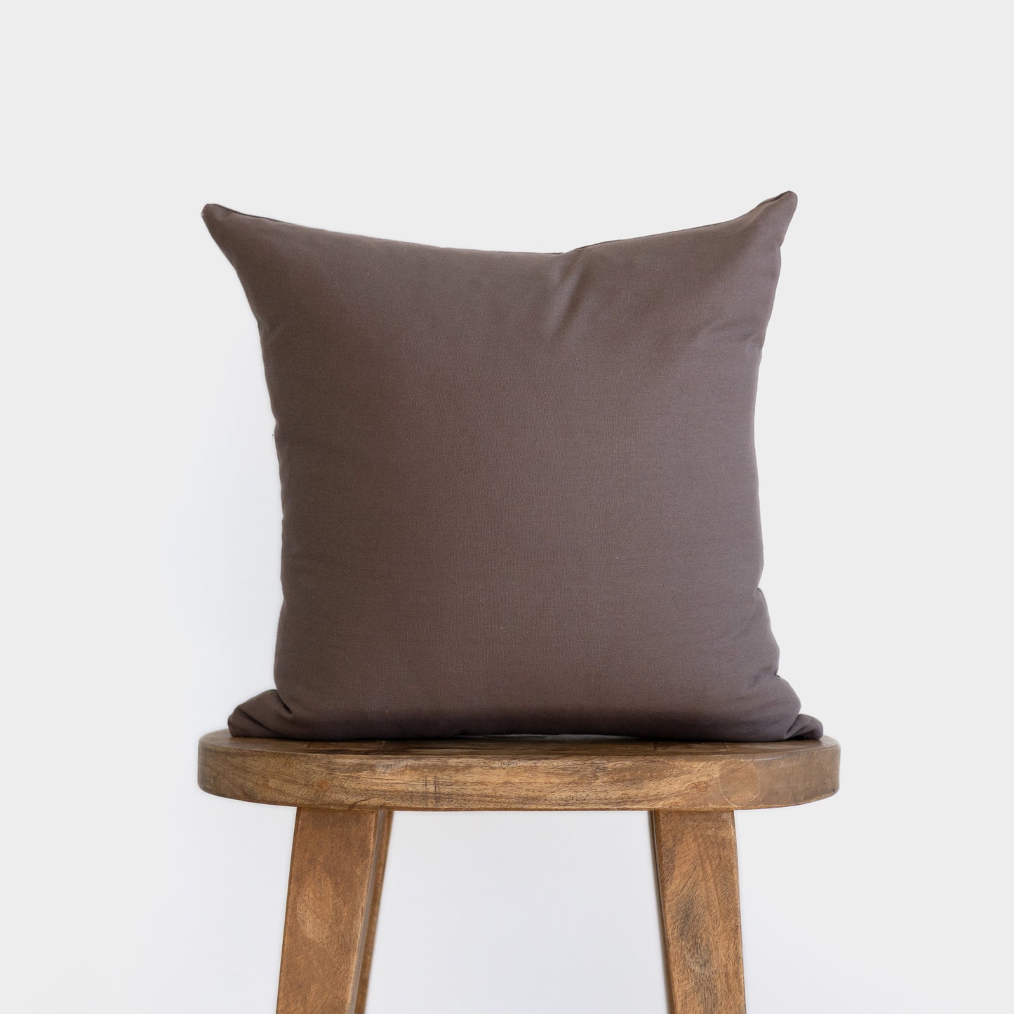 Mocha-brown square pillow with flange edges displayed on wooden stool.