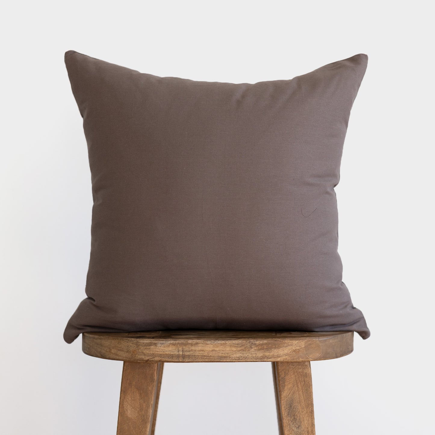 Mocha brown square pillow with solid linen texture displayed on wooden stool.