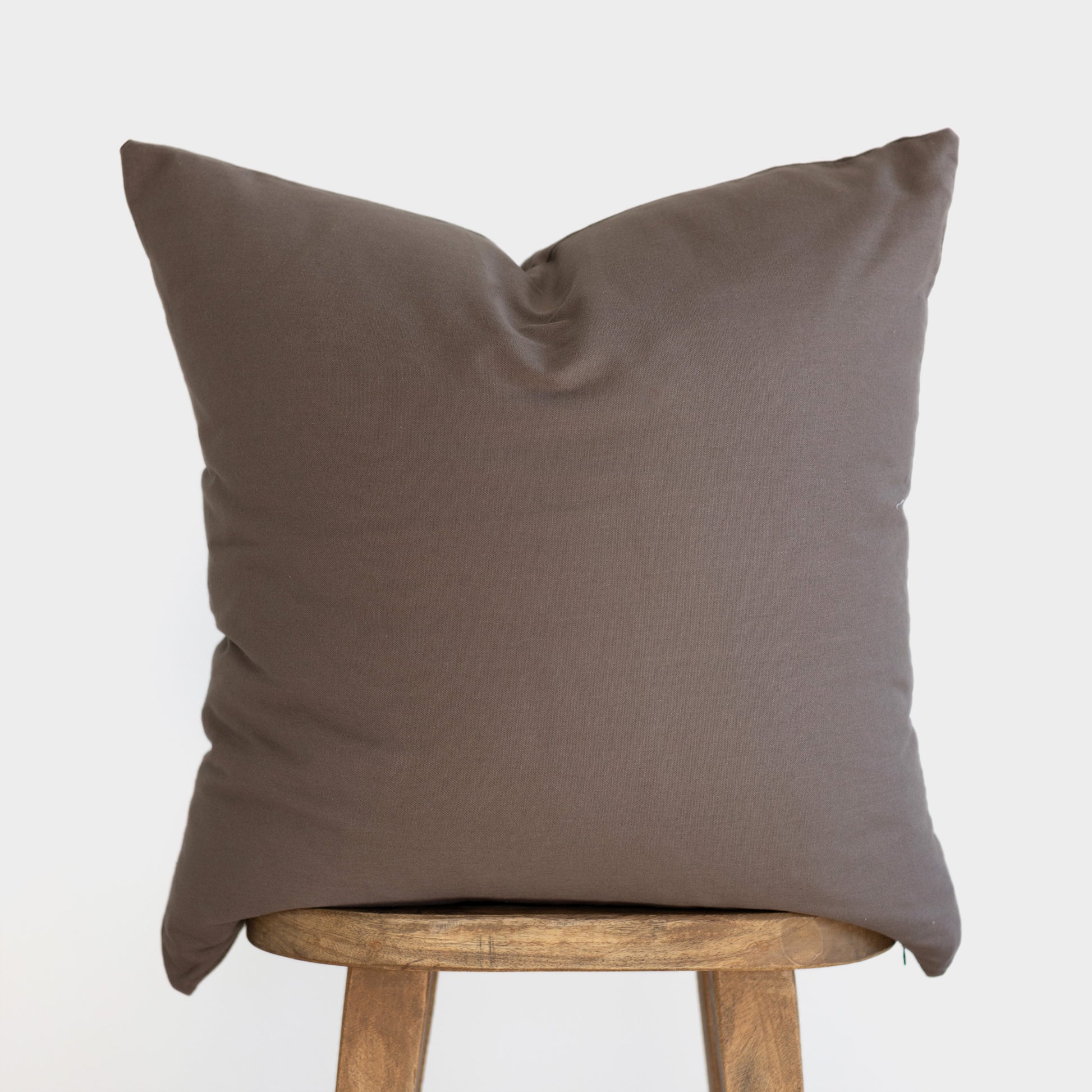 Mocha brown cushion cover with solid fabric displayed on wooden stool.