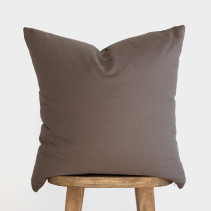 Mocha brown cushion cover with solid fabric displayed on wooden stool.