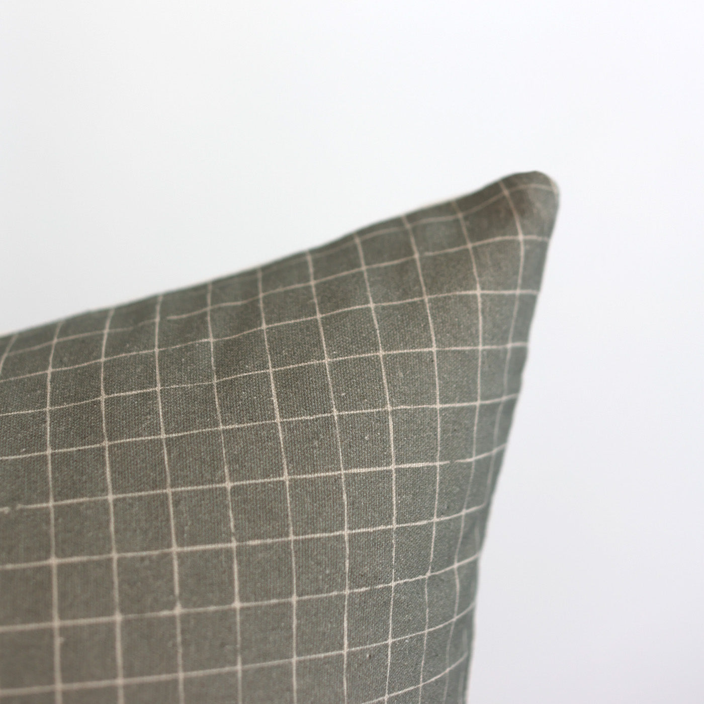 Moss-colored pillow with white grid pattern and rounded corner detail.
