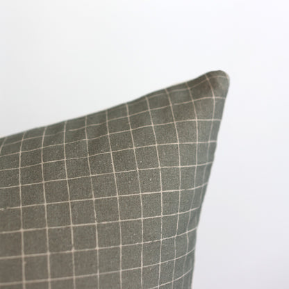 Moss-colored pillow with white grid pattern and rounded corner detail.