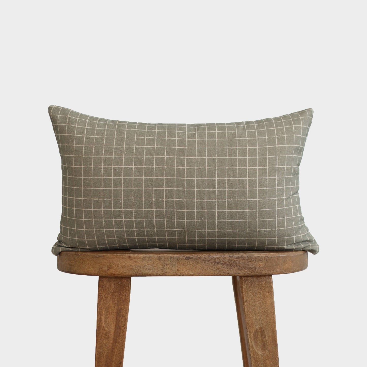 Moss green lumbar pillow with white grid pattern on wooden stool.