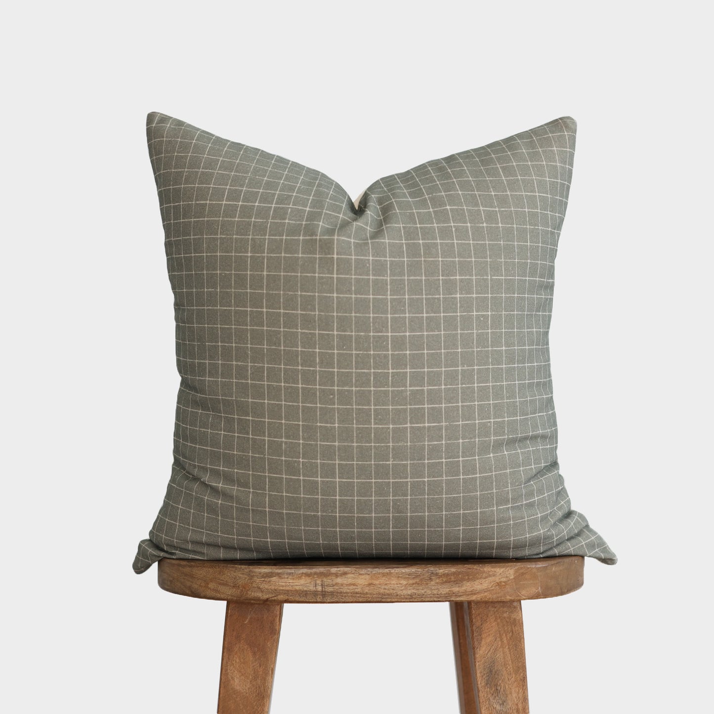 Moss green pillow with white grid pattern displayed on wooden stool.