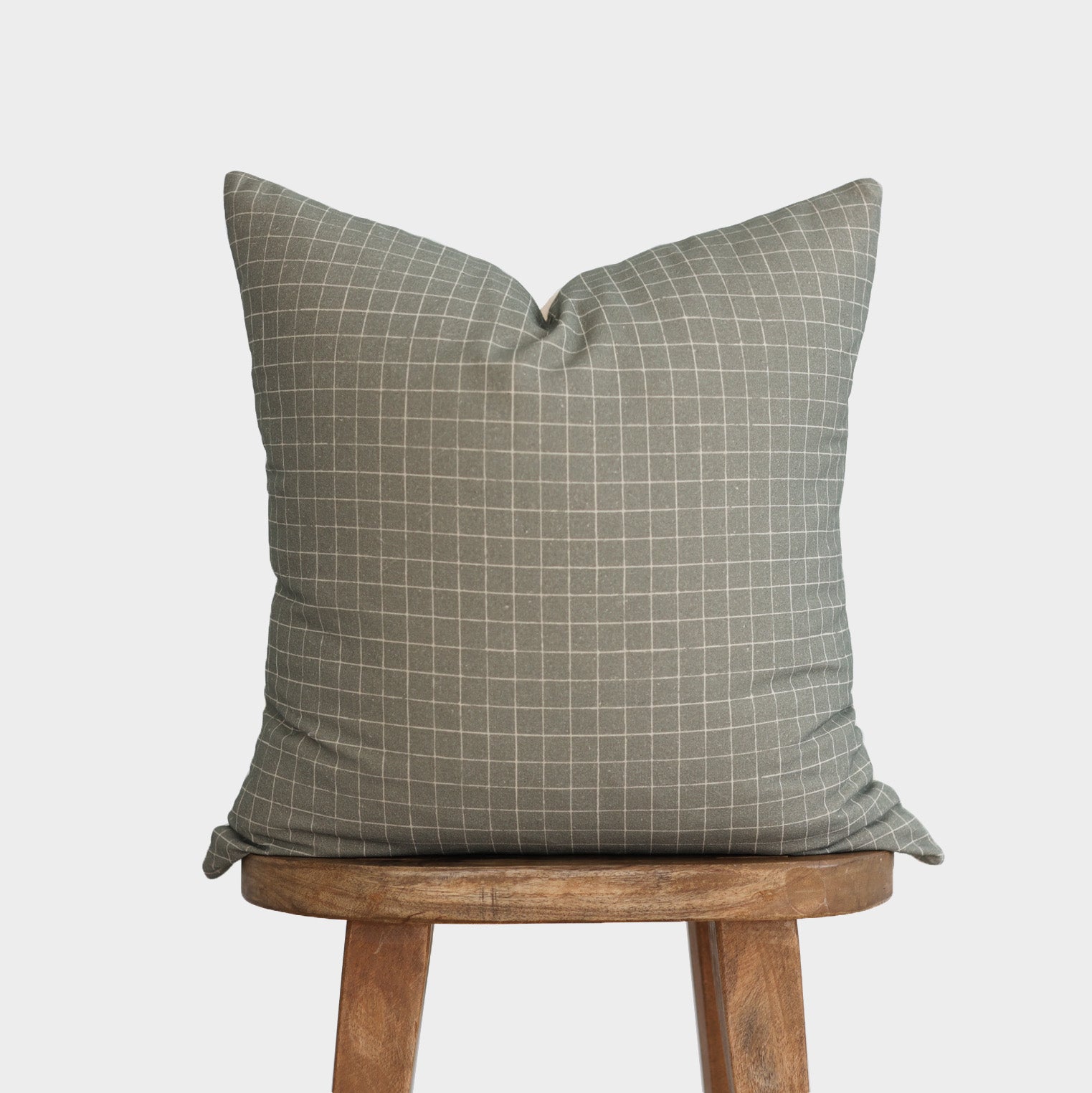 Moss green pillow with white grid pattern displayed on wooden stool.
