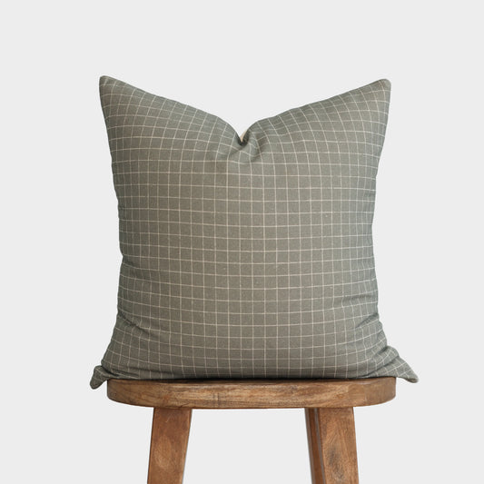 Moss green pillow with white grid pattern displayed on wooden stool.