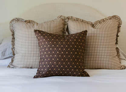 Decorative pillows in tan gingham and brown geometric patterns with ruffled edges arranged on a white bed.