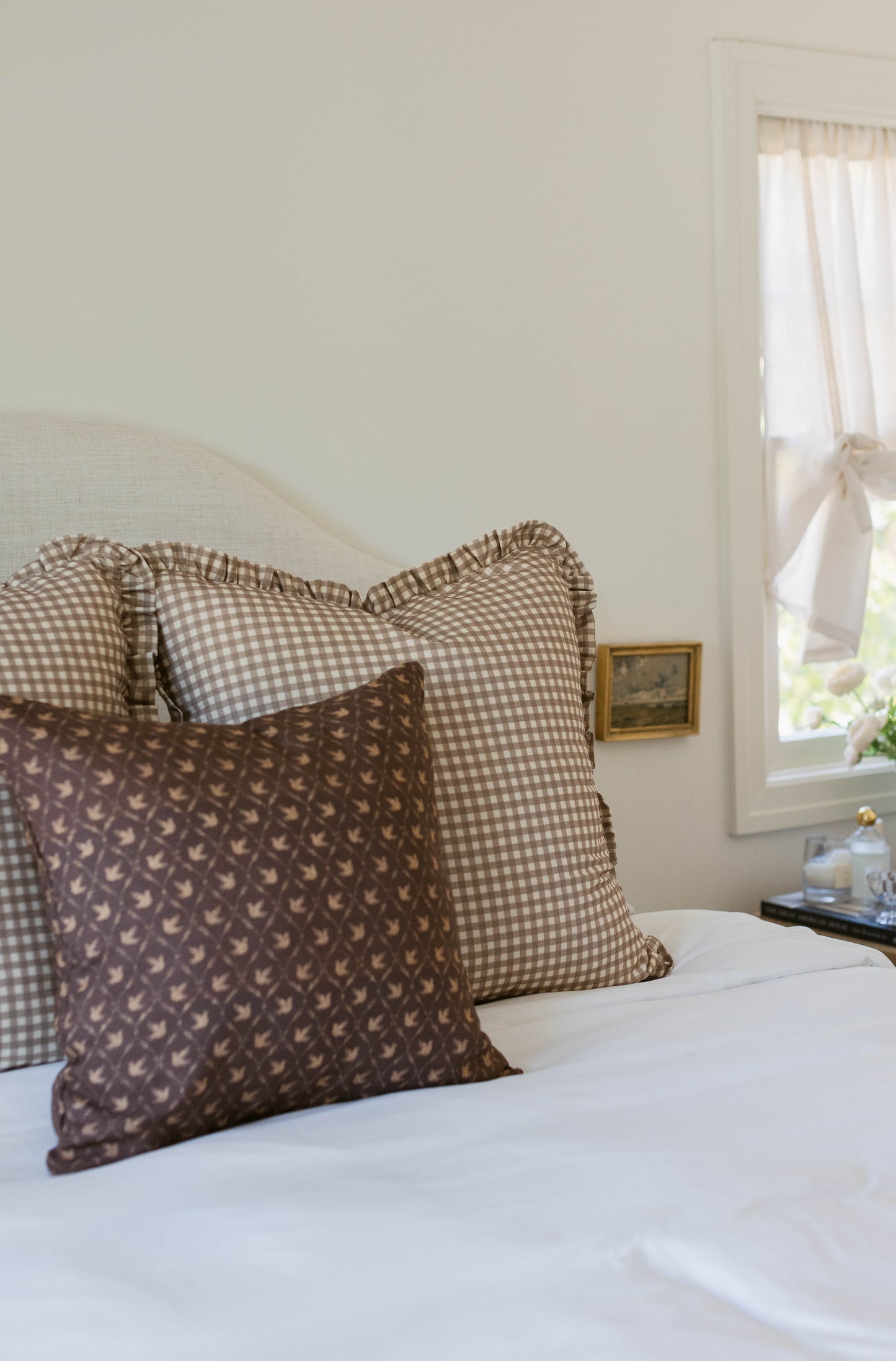 Tan and white gingham pillows with ruffled edges arranged on a bed.