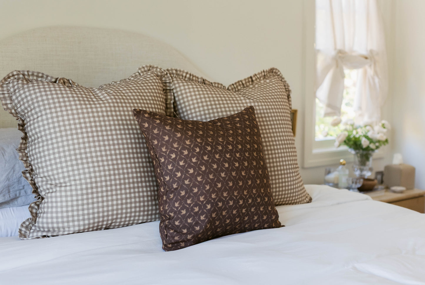 Brown patterned pillow with checkered gingham pillows on white bedding.