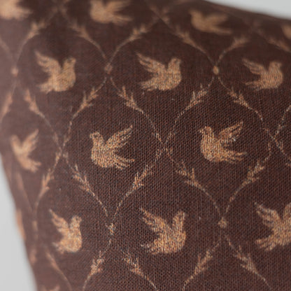 Brown pillow with gold dove pattern and textured fabric surface.