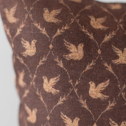 Brown cushion with tan dove silhouettes in a geometric lattice pattern.