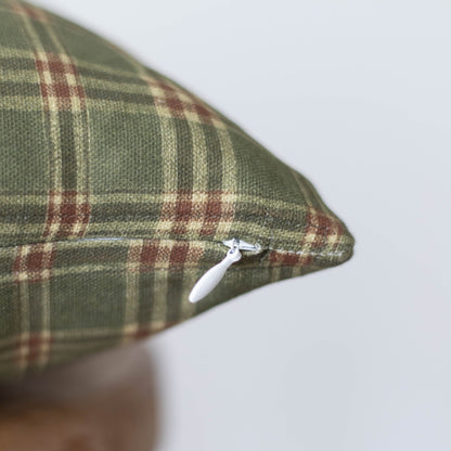 Green plaid cushion with red and cream tartan pattern and white zipper closure.