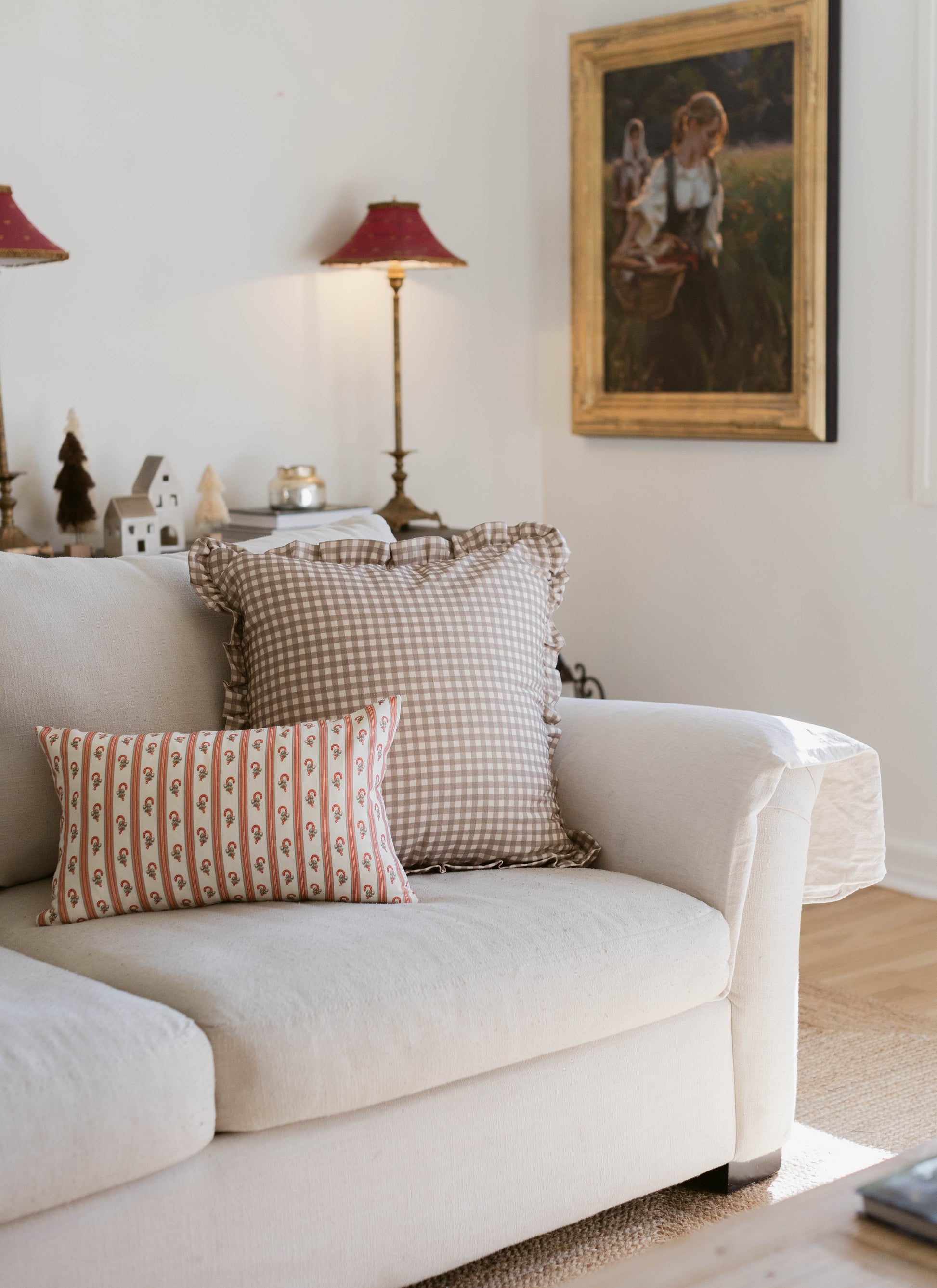 Tan and white gingham square pillow with ruffled edges displayed on a cream upholstered chair.
