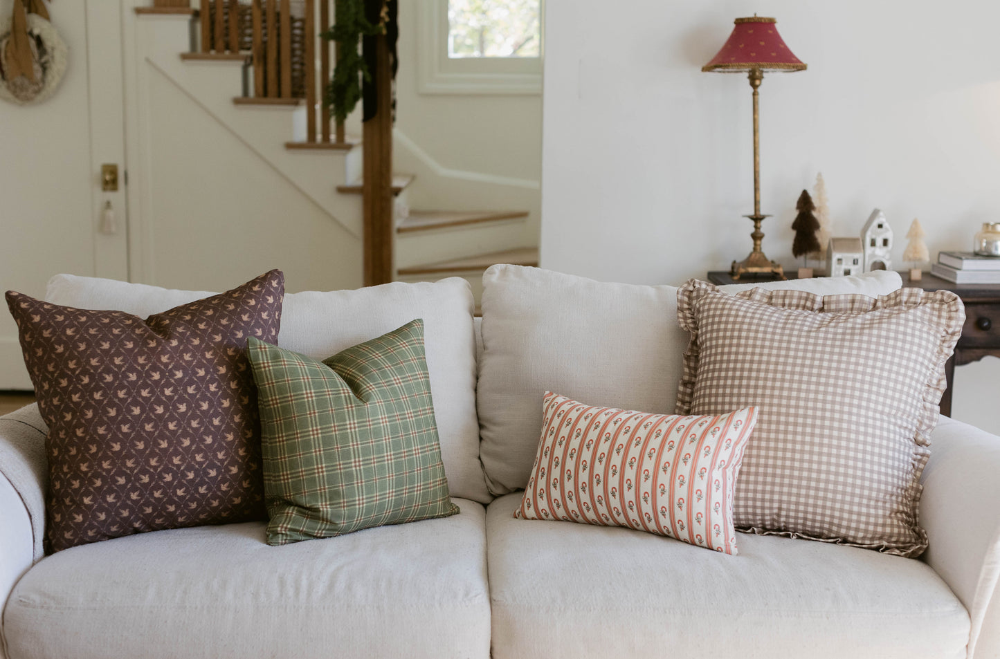 Cream-colored upholstered sofa with four decorative pillows in brown, green, coral, and beige patterns.