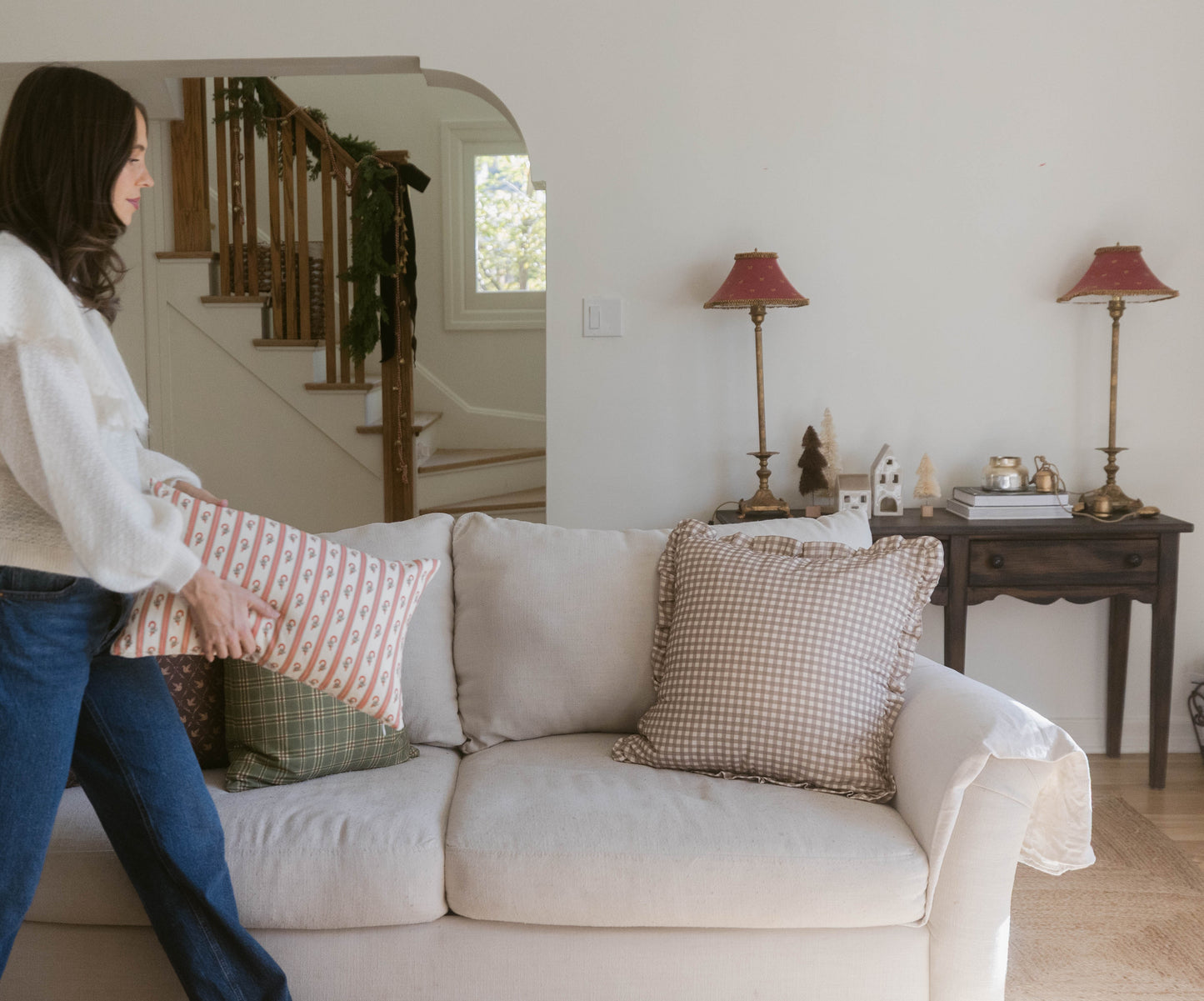 Tan and white gingham ruffle pillow displayed on a cream upholstered sofa next to a woman in a living room.