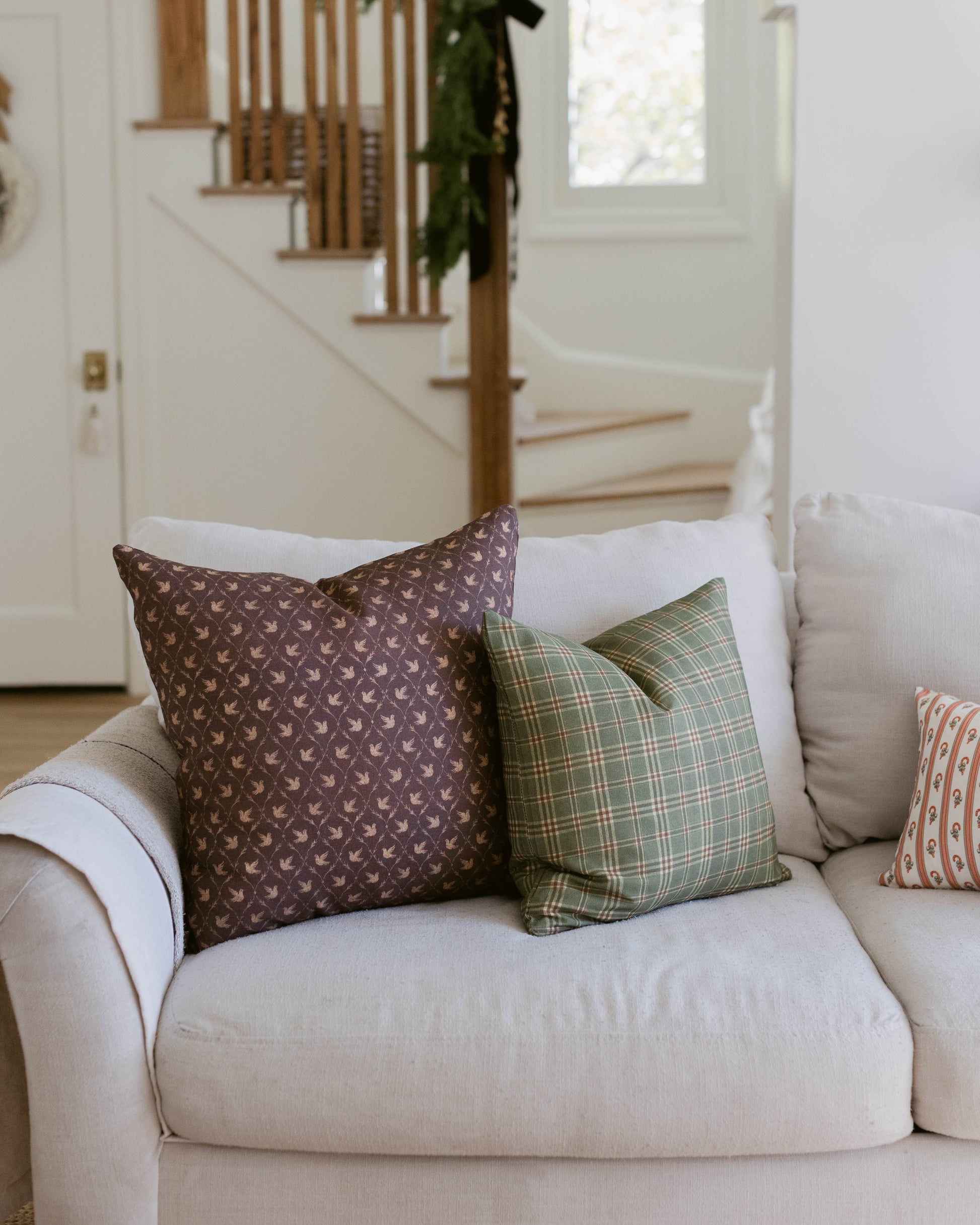 Brown patterned pillow with small repeated motif displayed on cream sofa with coordinating pillows.
