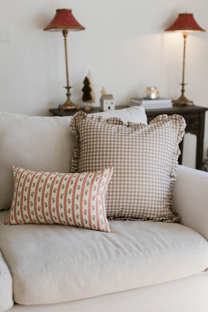 Tan and white gingham check pillow with ruffled edges displayed on a cream armchair.