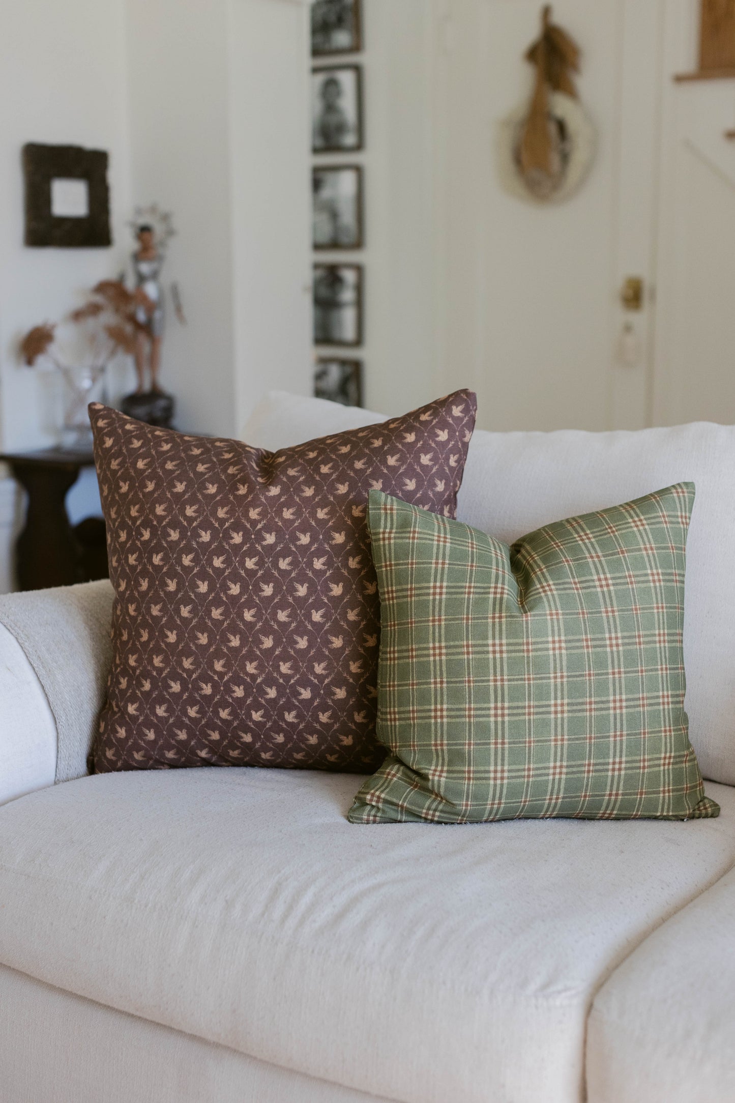 Brown leaf-patterned and green plaid throw pillows displayed on a cream-colored sofa.