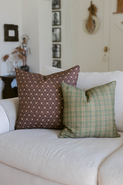 Brown leaf-patterned and green plaid throw pillows displayed on a cream-colored sofa.