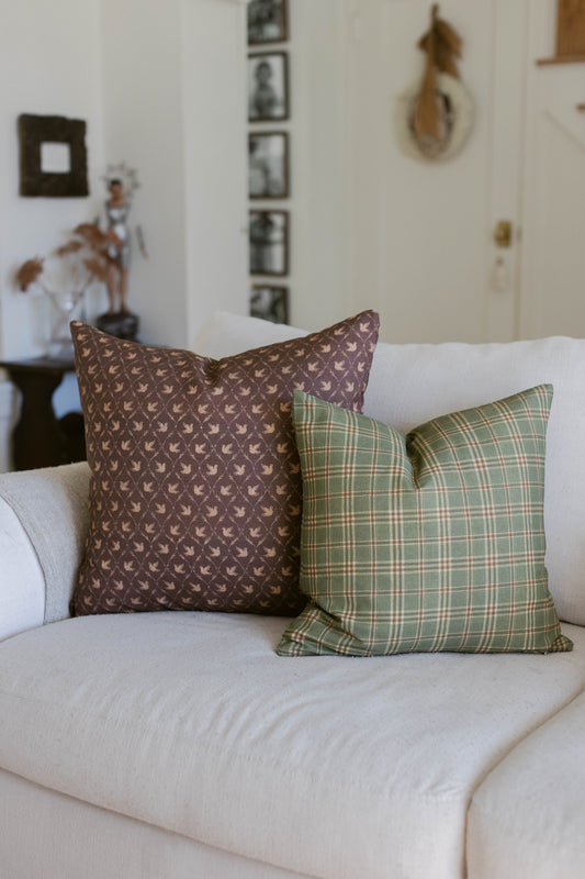 Brown leaf-patterned and green plaid throw pillows displayed on a cream-colored sofa.
