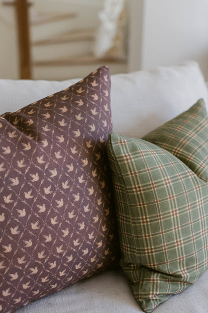 Purple pillow with bird pattern and green plaid pillow displayed on white bedding.