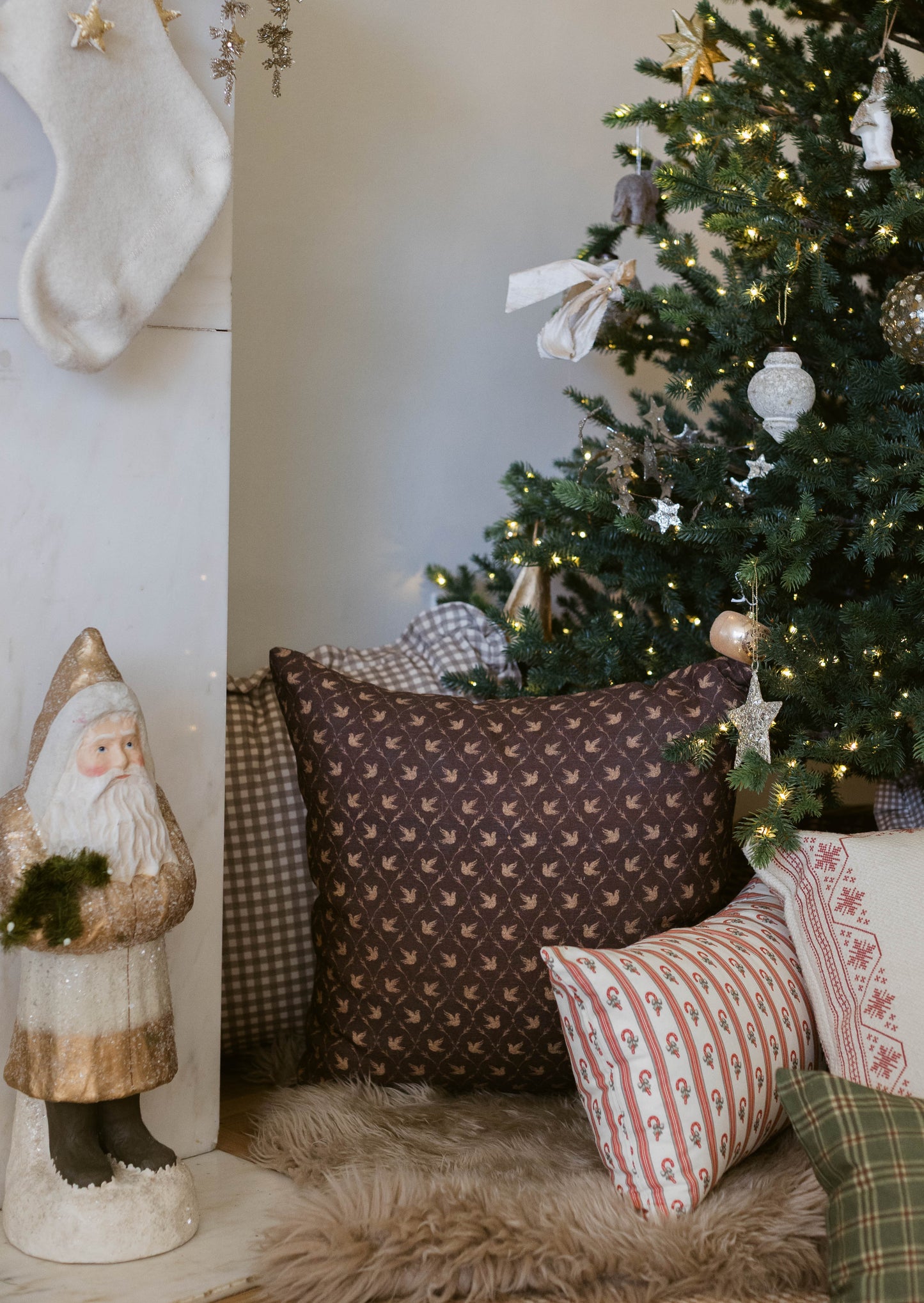 White knit stocking with gold star ornaments hanging on wall beside decorated Christmas tree.