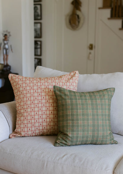 Two decorative pillows on a cream sofa: one with red tree pattern on cream background, one with green plaid pattern.