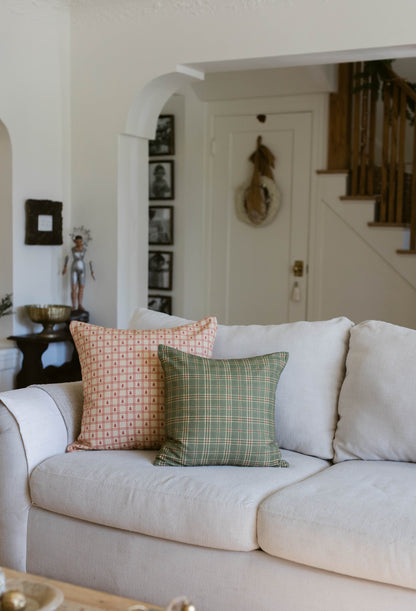 Cream upholstered sofa with orange patterned and green plaid throw pillows in a living room with arched doorway and staircase