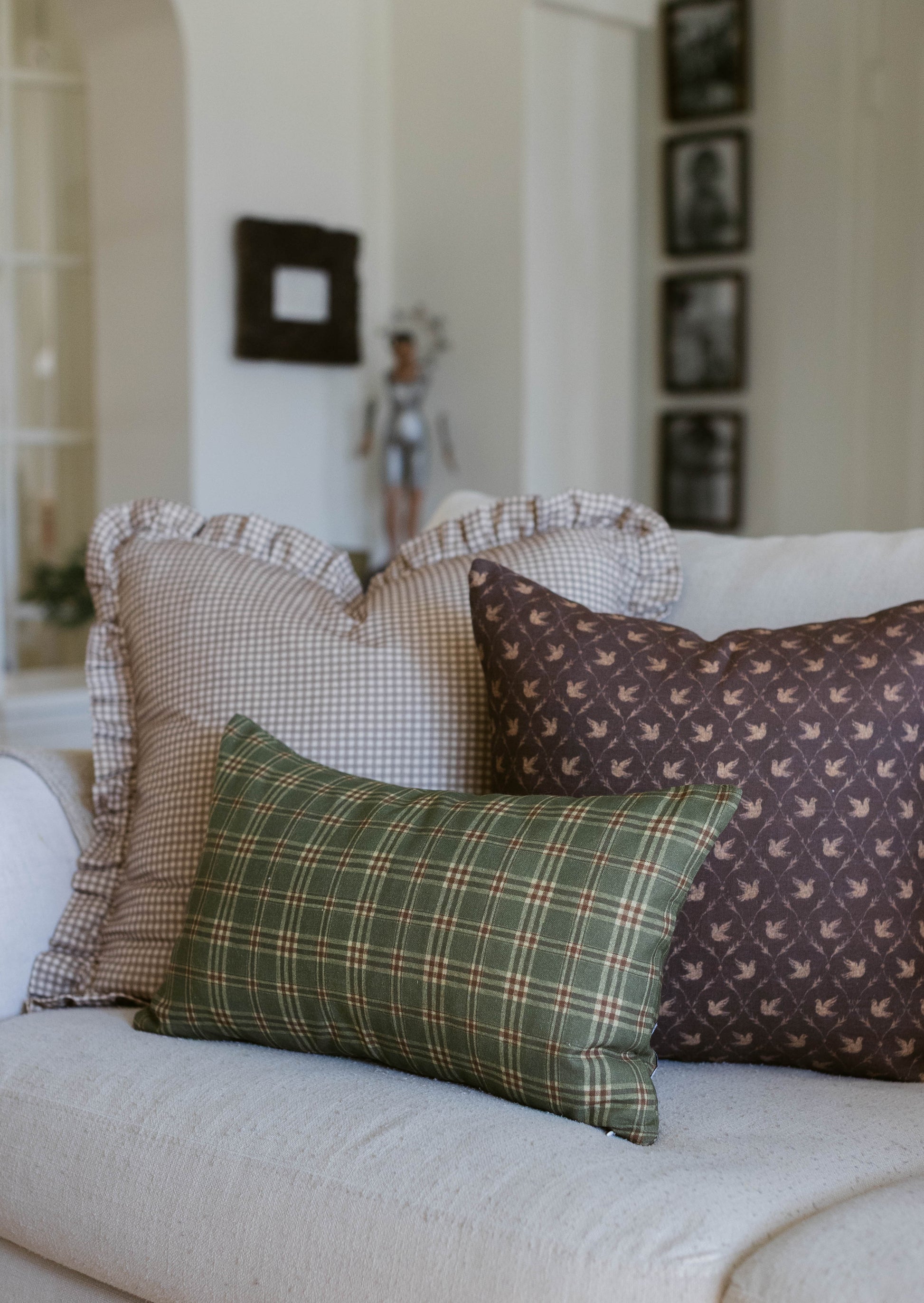 Green plaid pillow with brown bird-print and beige gingham pillows arranged on a white bed.