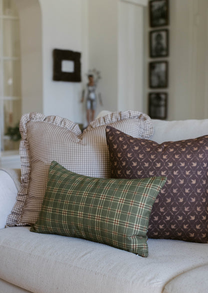 Green plaid pillow with brown bird-print and beige gingham pillows arranged on a white bed.