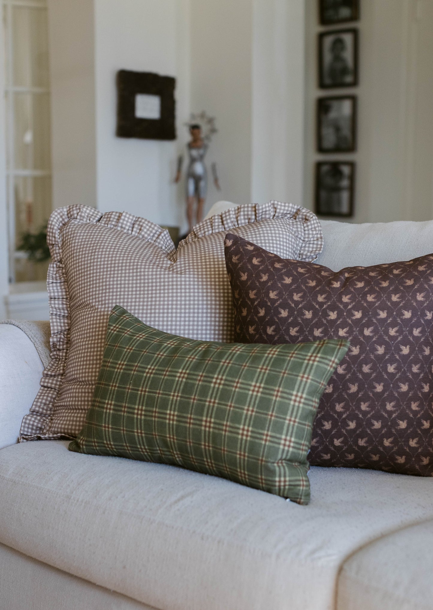 Three decorative pillows with checkered and bird patterns arranged on a light-colored sofa.