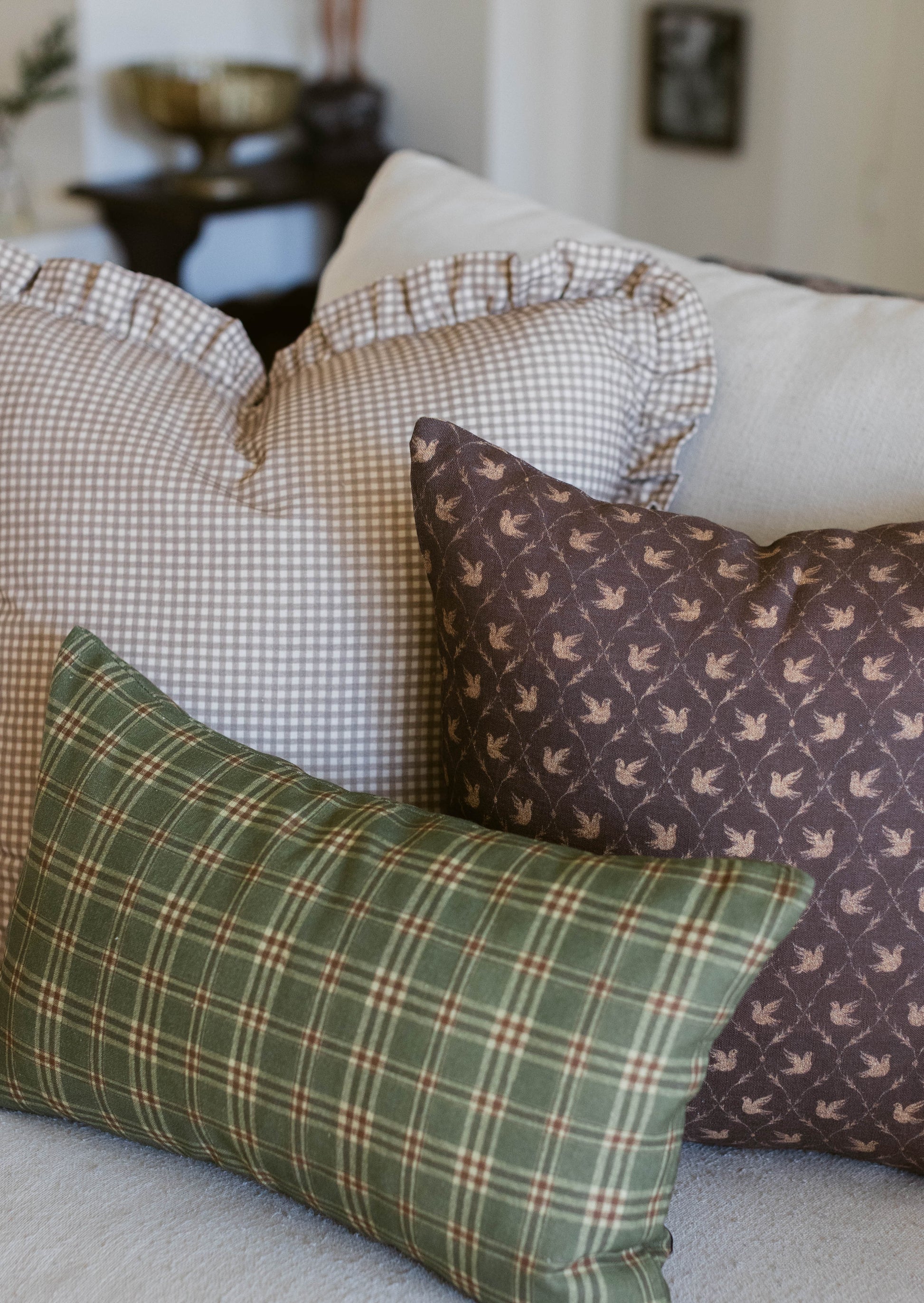 Three decorative pillows with gingham, plaid, and bird patterns arranged on a cream sofa.