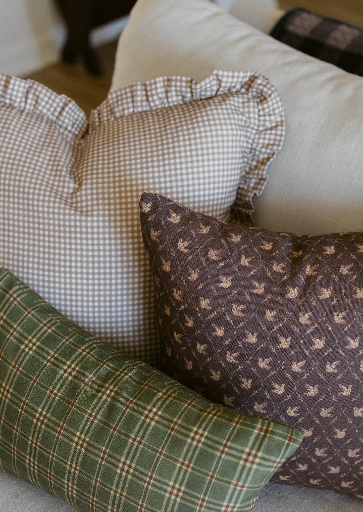 Tan and white gingham pillow with ruffled edges displayed among other patterned throw pillows on a couch.
