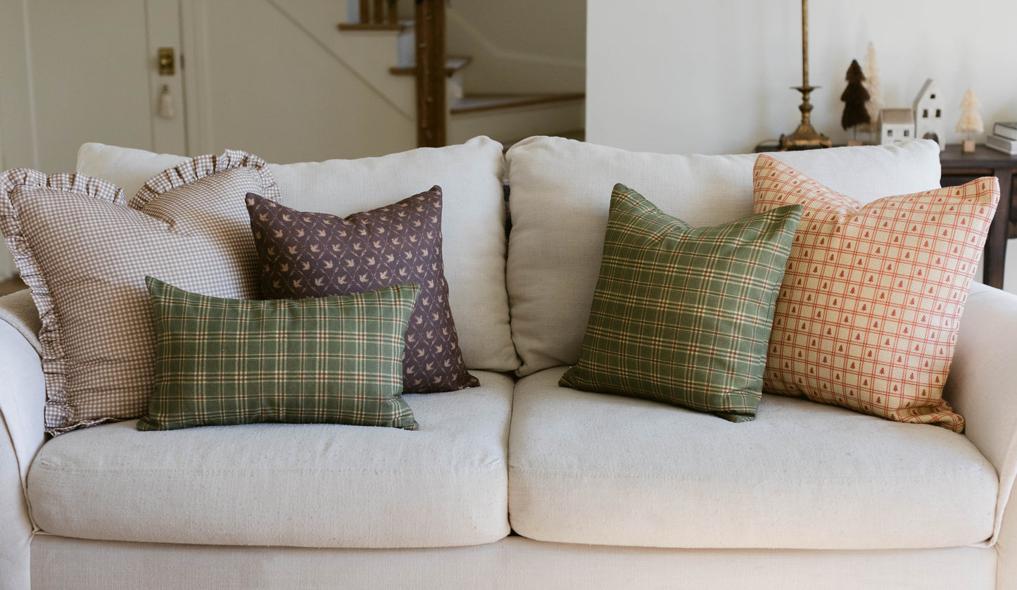Cream upholstered sofa with five decorative pillows in plaid, geometric, and checkered patterns in green, brown, and coral to