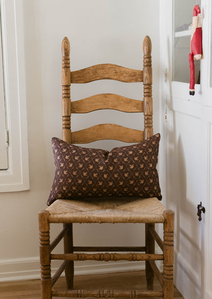 Wooden ladder-back chair with woven rush seat and brown patterned pillow.