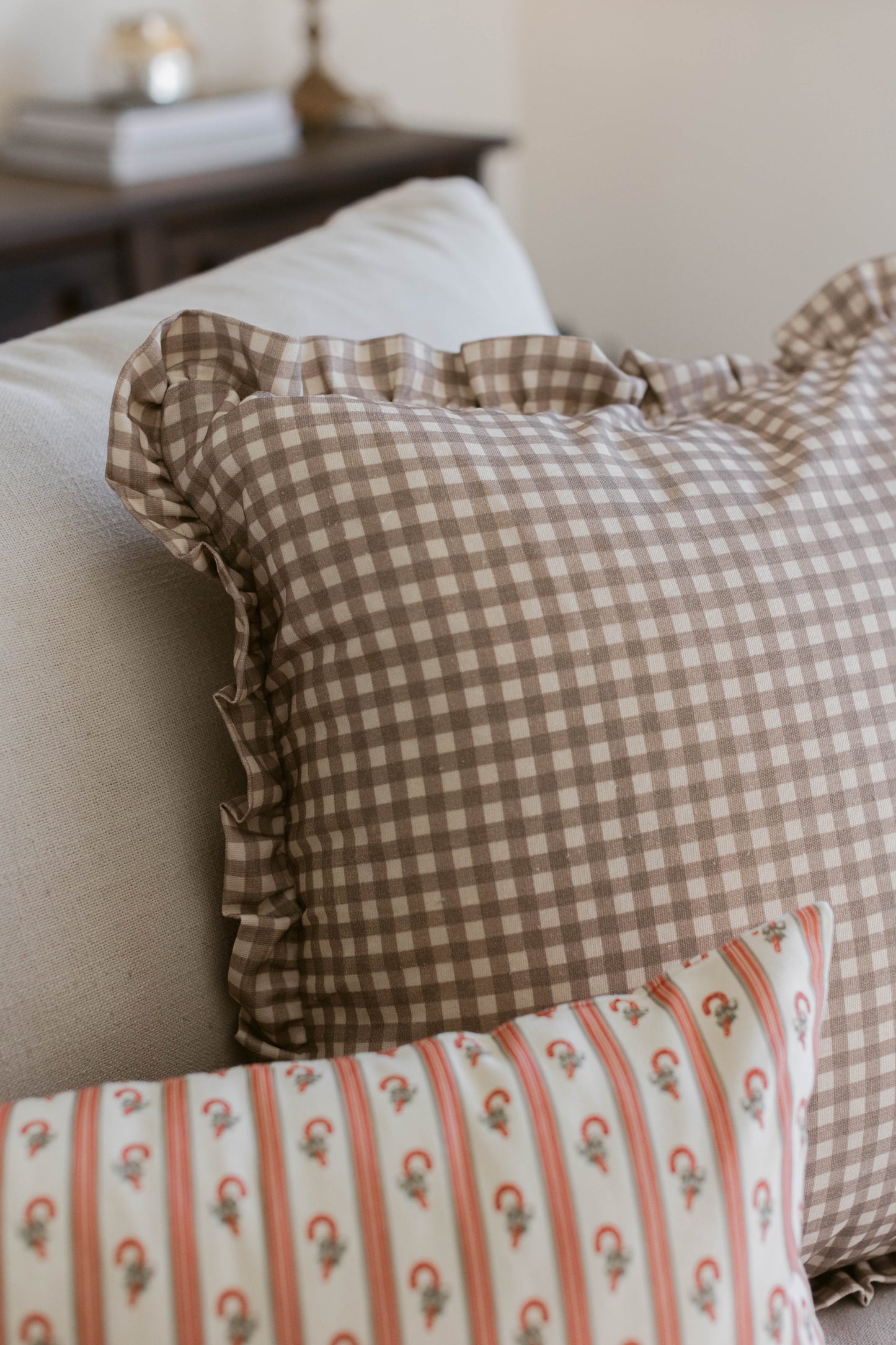 Tan and white gingham pillow with ruffled edges on a bed.