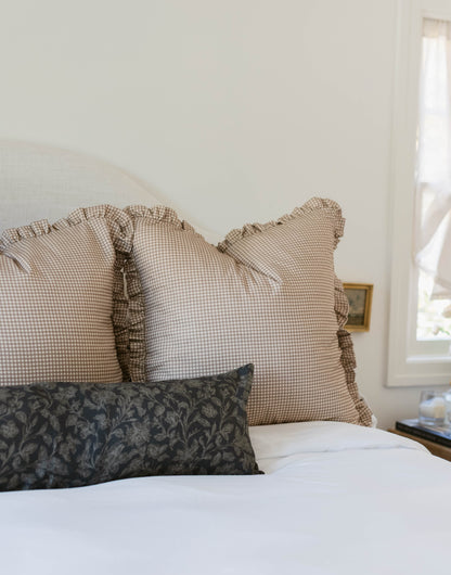 Tan and white mini gingham pillows with ruffled edges displayed on a bed.