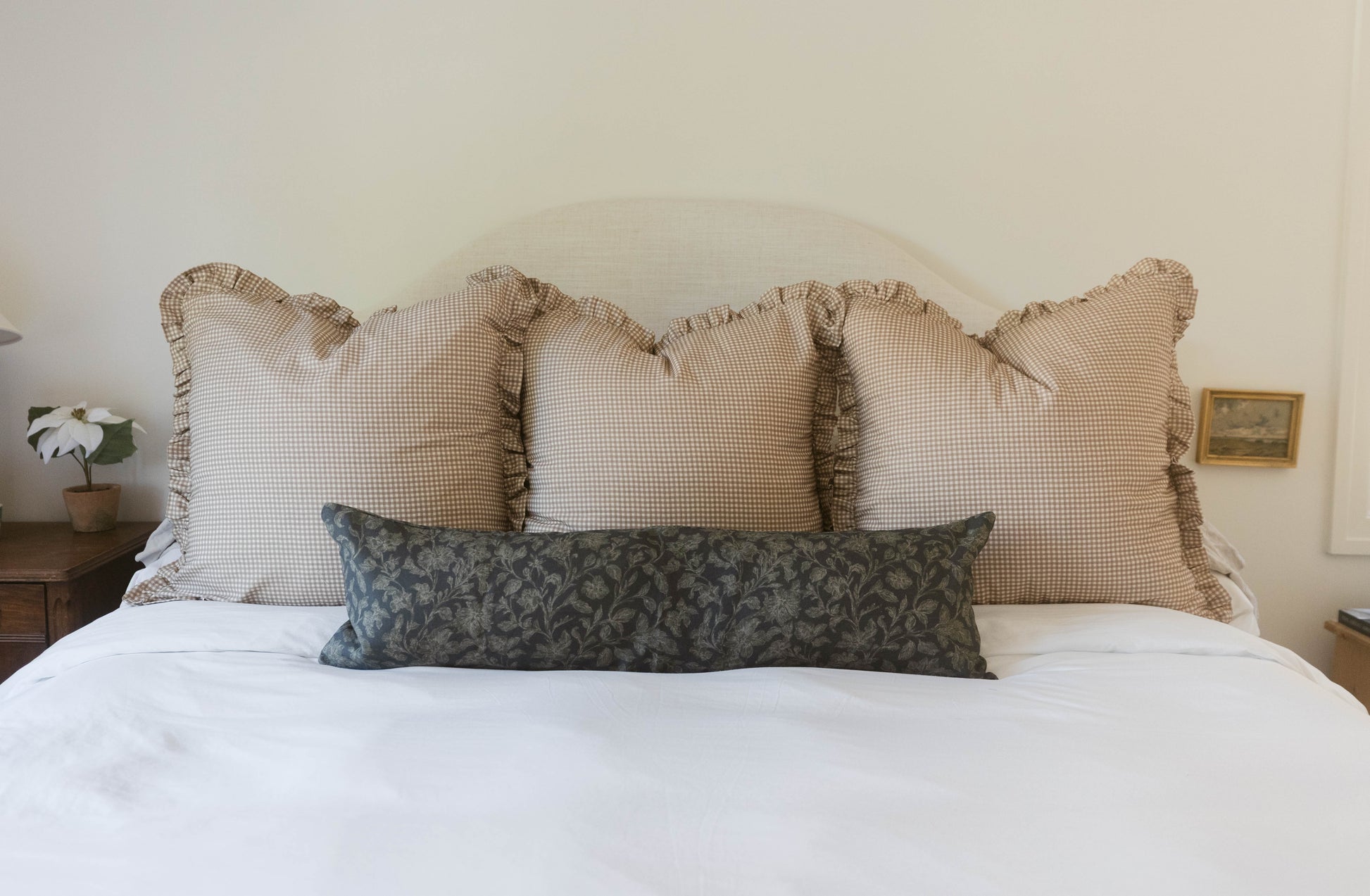 Tan and white gingham pillows with ruffled edges arranged on a bed.